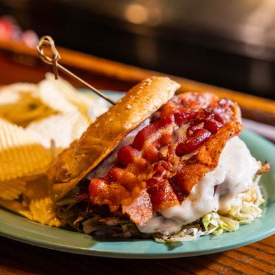 Sicilian Chicken Sandwich topped with melted cheese and bacon, served with chips.