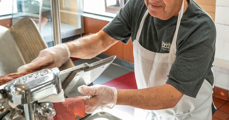 Kitchen staff member slicing meat on a meat slicer
