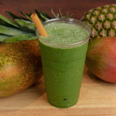 Green Lantern smoothie cup displayed with pineapple, papaya and mango on the table.
