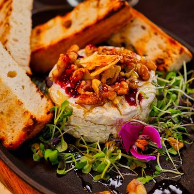 Baked camembert cheese topped with nuts, served with toasted bread and microgreens.