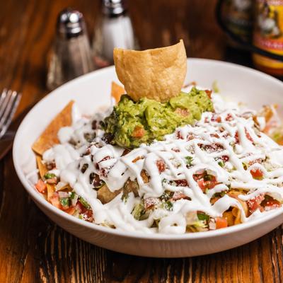 Serving of fully loaded nachos topped with guacamole and sour creeme.