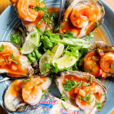 A plate of fresh oysters on the half shell topped with shrimp and cocktail sauce.