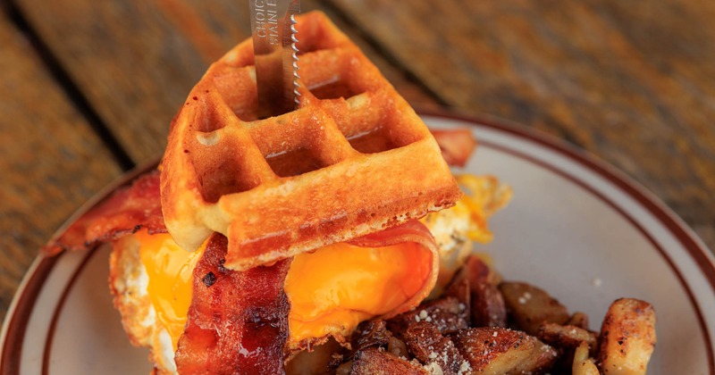 Waffle sandwich filled with fried eggs, bacon, and melted cheddar cheese