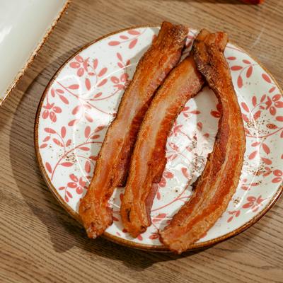 A plate with three strips of smoked bacon on it.