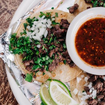 Steak tacos with onions, cilantro, lime wedges, and salsa on the side.