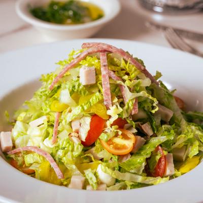 Chopped salad with lettuce, tomatoes, and salami slices.