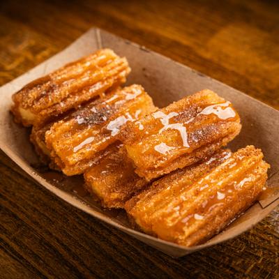 Churros drizzled with caramel sauce, served in a paper container.