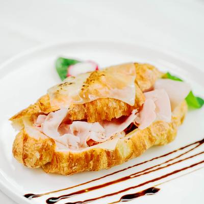 Croissant sandwich with ham and melted cheese on a white plate with balsamic glaze.