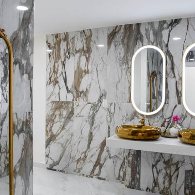Bathroom featuring marble walls, gold accents, and oval mirrors.