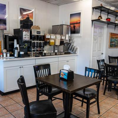 Interior with a beverage station, tables, chairs, and framed sunset photographs.