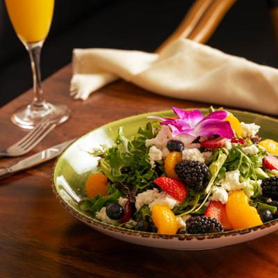 A salad with fruit and a glass of Mimosa.