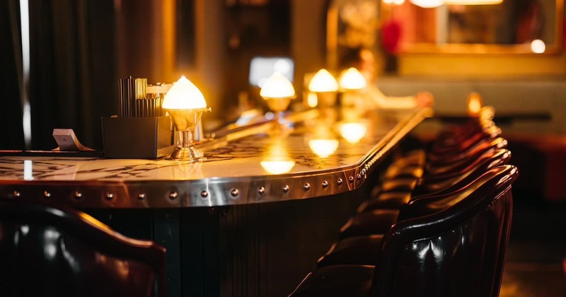 Row of shiny leather bar stools next to a polished bar with lamps and drink accessories