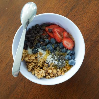 Breakfast bowl with mixed berries, yoghurt, granola, honey, chia seeds, and chocolate chips.