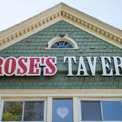 Rose's Tavern sign mounted on a green shingled building facade.