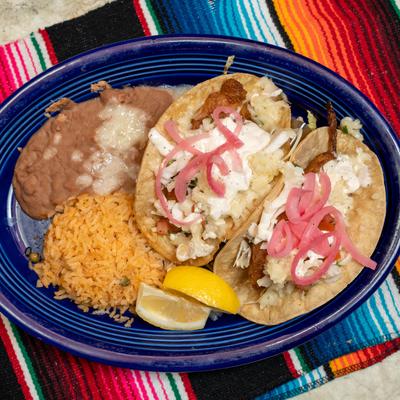 Two fish tacos with pickled onions, rice, and beans on blue plate.