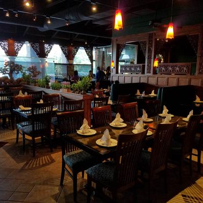 Elegant restaurant interior with wooden chairs, neatly set tables, warm pendant lighting, and decorative greenery.