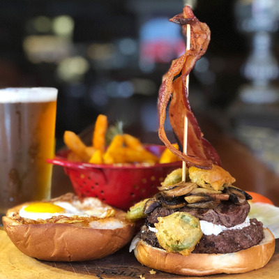 An open-faced burger stacked with bacon, mushrooms, and fried pickles.