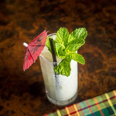 White cocktail with crushed ice, fresh mint, and a red cocktail umbrella.