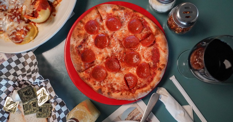 Small pepperoni pizza on a red tray with condiments
