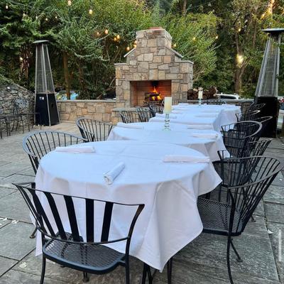 Lined up clothed tables in the patio with patio heaters and a fireplace in the back