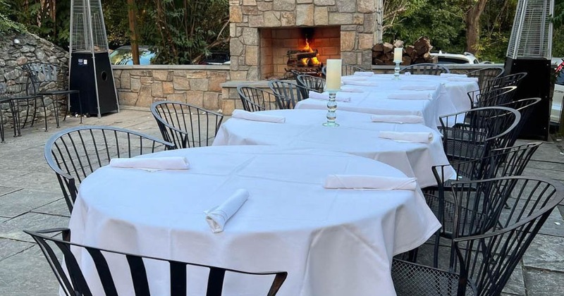 Lined up clothed tables in the patio with patio heaters and a fireplace in the back