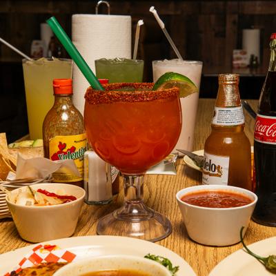 A table spread featuring a michelada surrounded by various beverages and appetizers.