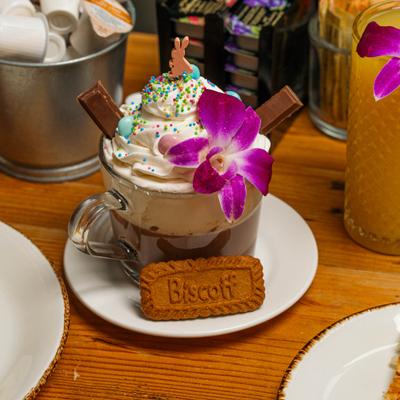 Hot Chocolate topped with whipped cream, sprinkles, a Biscoff cookie, and a purple orchid.