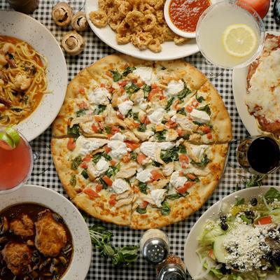 Assortment of Italian dishes and drinks spread on a table, with a large pizza in the center.