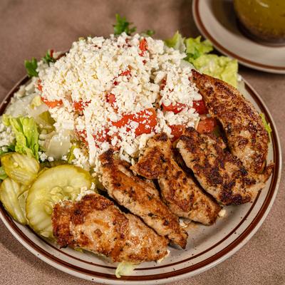 Grilled chicken strips atop a salad with tomatoes, lettuce, pickles, and cheese.