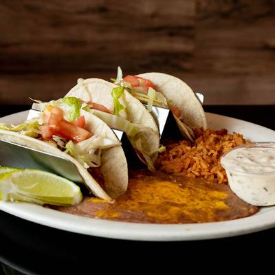 Grilled fish tacos served with a sauce, rice and refried beans.