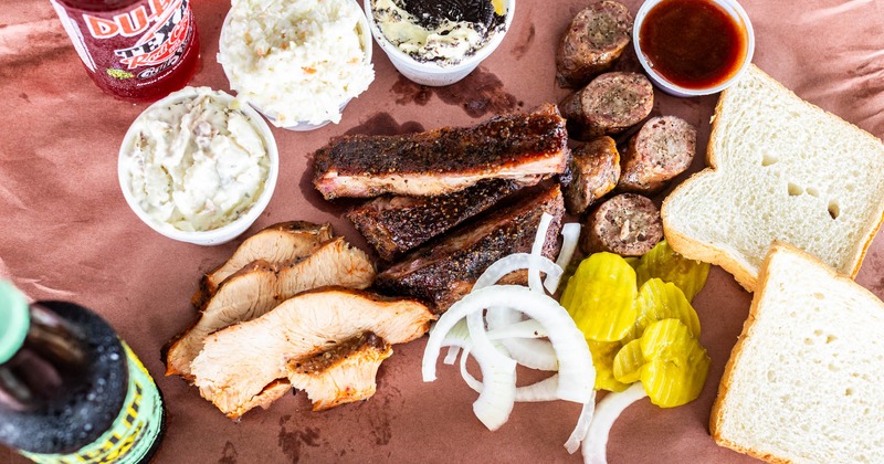 Ribs, sausage, sliced turkey, pickles, onions, potato salad, and bread, with soda bottles