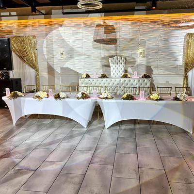Elegant event setup featuring a white tufted head table with gold accents and floral arrangements.