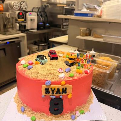 Pink birthday cake decorated with toy cars and crumb sand.