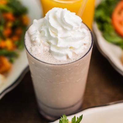 A milkshake glass surrounded by assorted food plates, close up.