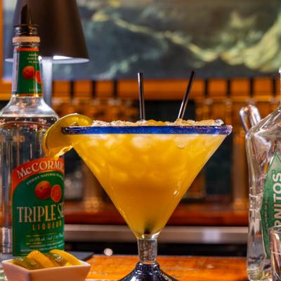 Grande Margarita cocktail alongside spirit bottles and small boel of garnishes.