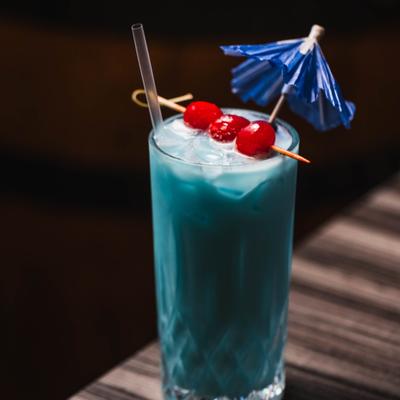 Bella Blue cocktail garnished with cherries and a paper umbrella.