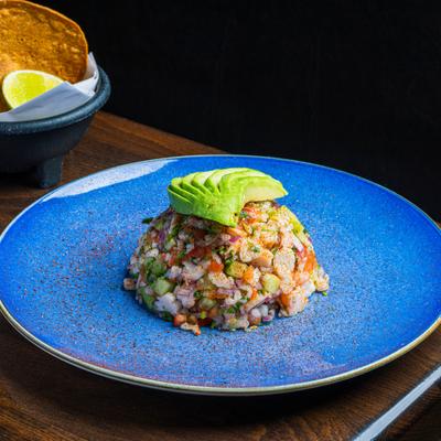 Ceviche topped with avocados slices on a blue plate.