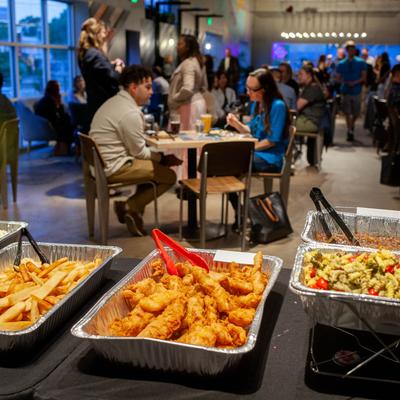 Catering trays on a table at an indoor event, guests dining in the background.