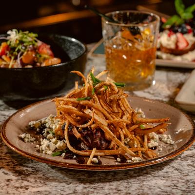 Steak Frites served on the table alongside a cocktail and other dishes.