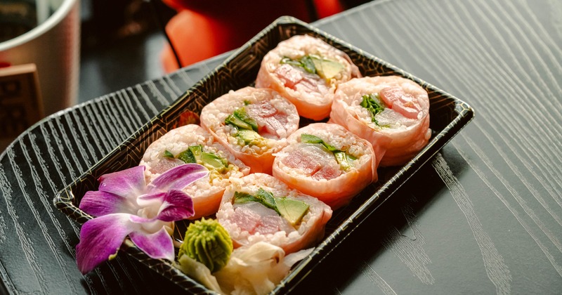 Fresh sushi rolls wrapped in pink paper with tuna, avocado, and flowers