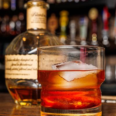 Old Fashioned cocktail sits on a bar counter with a bottle of whisky.