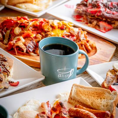 A breakfast spread, a teal coffee mug at the center, surrounded by food plates.