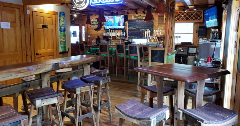 Bar with wooden tables, stools, TVs, and neon signs