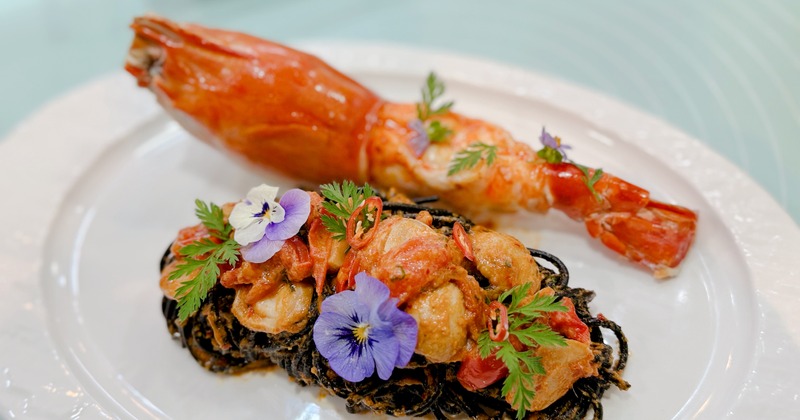 Squid ink pasta topped with edible flowers and accompanied by a large prawn