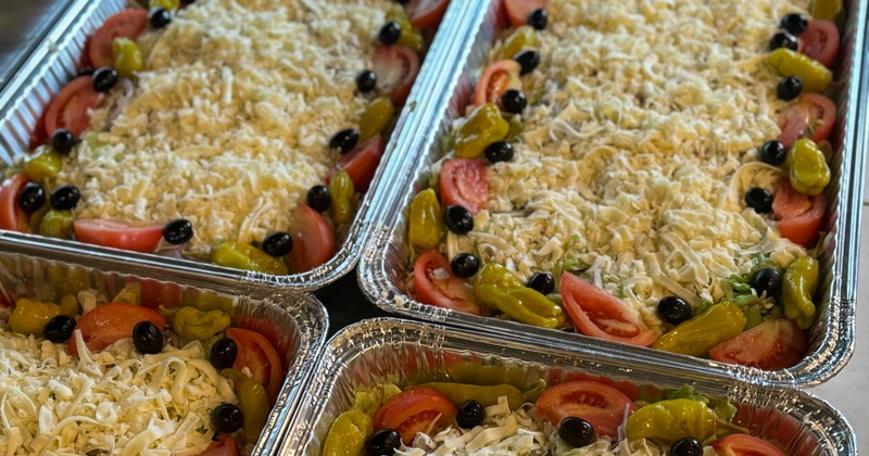 Multiple aluminum catering trays filled with salads