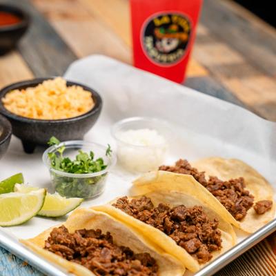 Street tacos served with sides of rice, fresh cilantro, lime wedges, and onions.