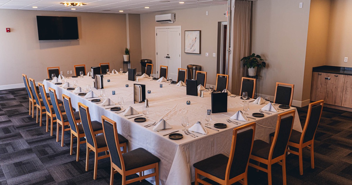 Formally set dining room, long table, white tablecloth, wooden chairs, plates, silverware