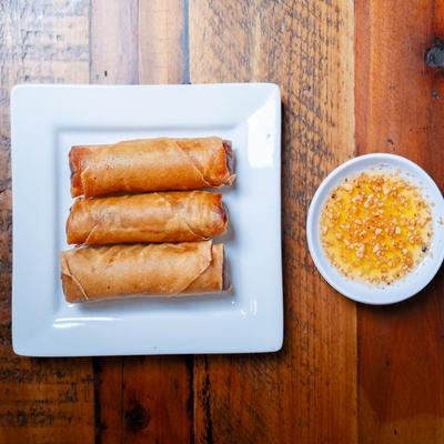 Three pork egg rolls served on a white plate with peanut sauce on the side.