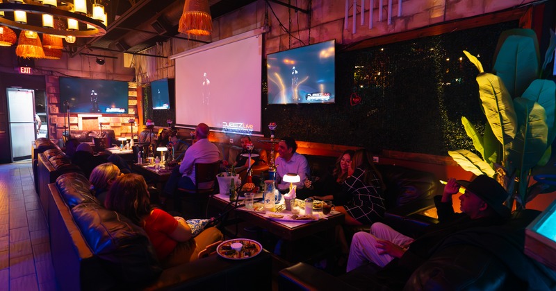 Interior, booths, couches, coffee tables, people sitting, tv screens above
