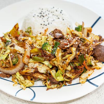Beef stir fried with vegetables, served with rice on the side.